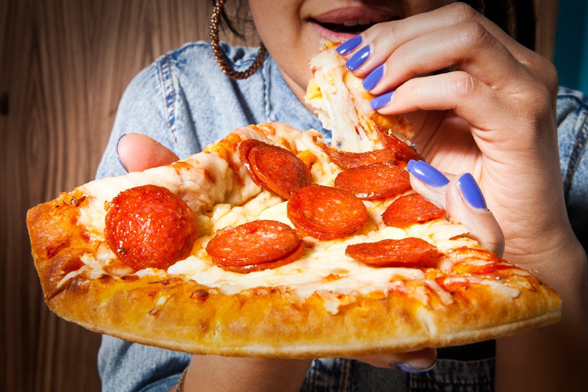 Pessoa comendo um pedaço generoso de pizza de muçarela com rodelas de pepperoni